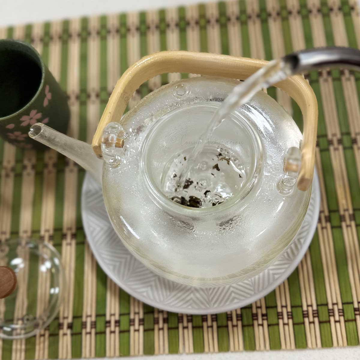 Pouring hot water over tea leaves in glass teapot